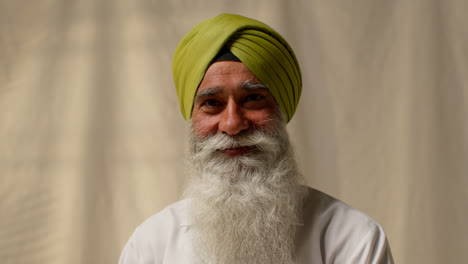 Studio-Portrait-Shot-Of-Smiling-Senior-Sikh-Man-With-Beard-Wearing-Turban-Against-Plain-Background